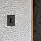 Bronze Black 1G Two Way Rocker Switch mounted on a beige wall next to a wooden doorframe.