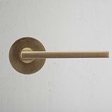 Antique brass Clayton Flush Rose Sprung door handle on textured white wall.