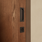 Bronze Regent pull and black flush lock on a wooden sliding door against a beige wall.