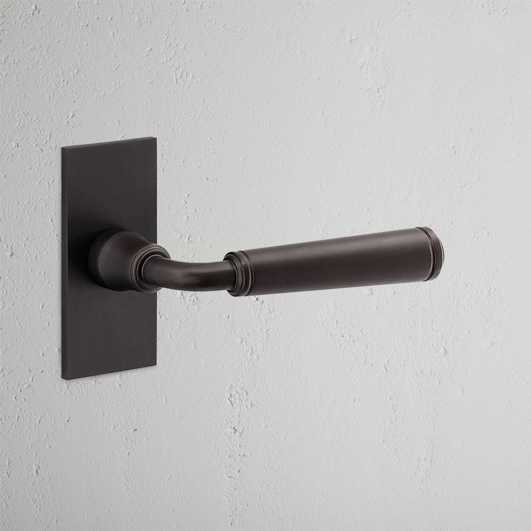 Digby Short Plate Fixed Door Handle in bronze, mounted on a light-colored surface.