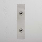 Polished Nickel 2G Architrave Two Way Toggle Switch with two round toggles on a white textured wall panel.