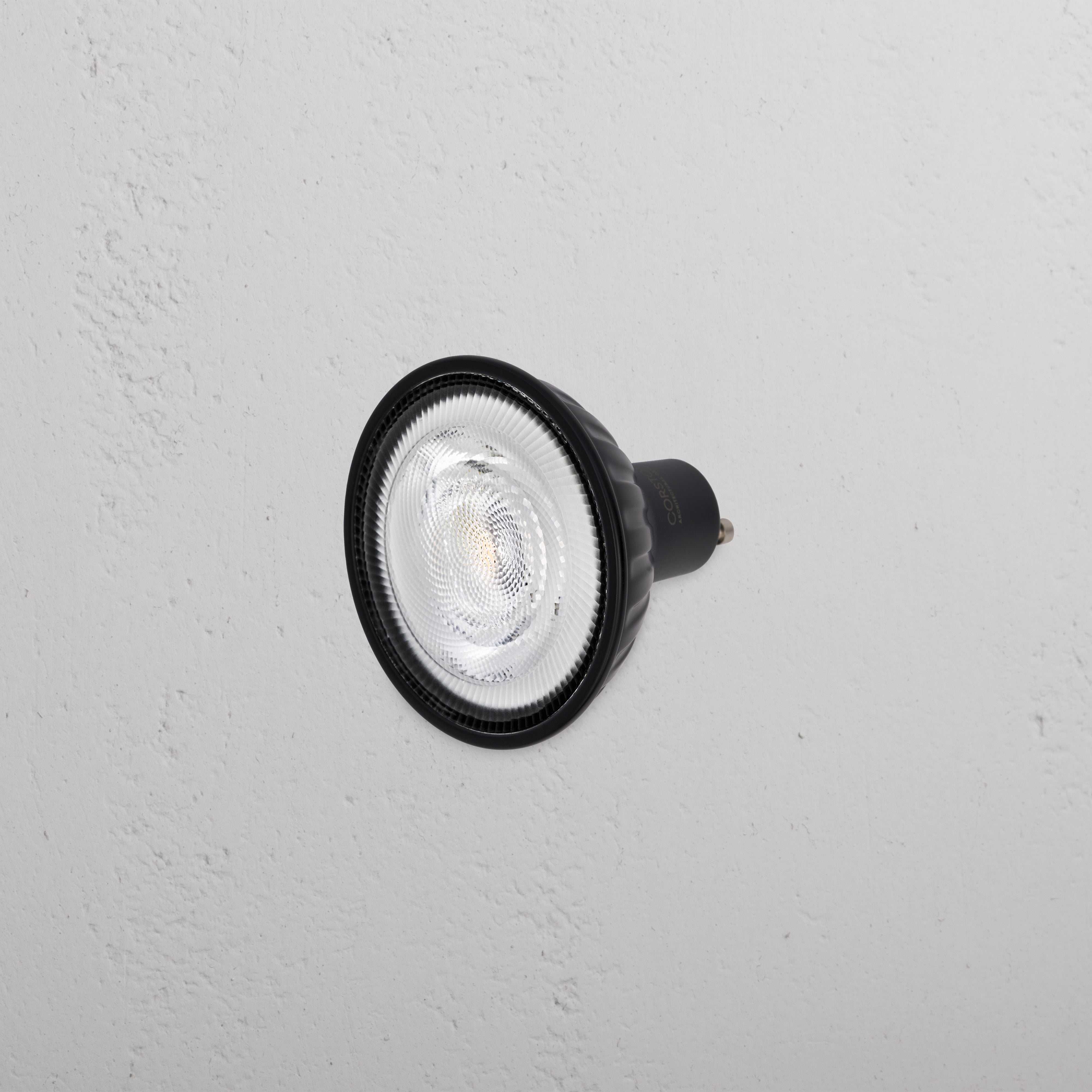 Arthur 70mm GU10 LED Bulb 24° in black, mounted on a textured white wall.