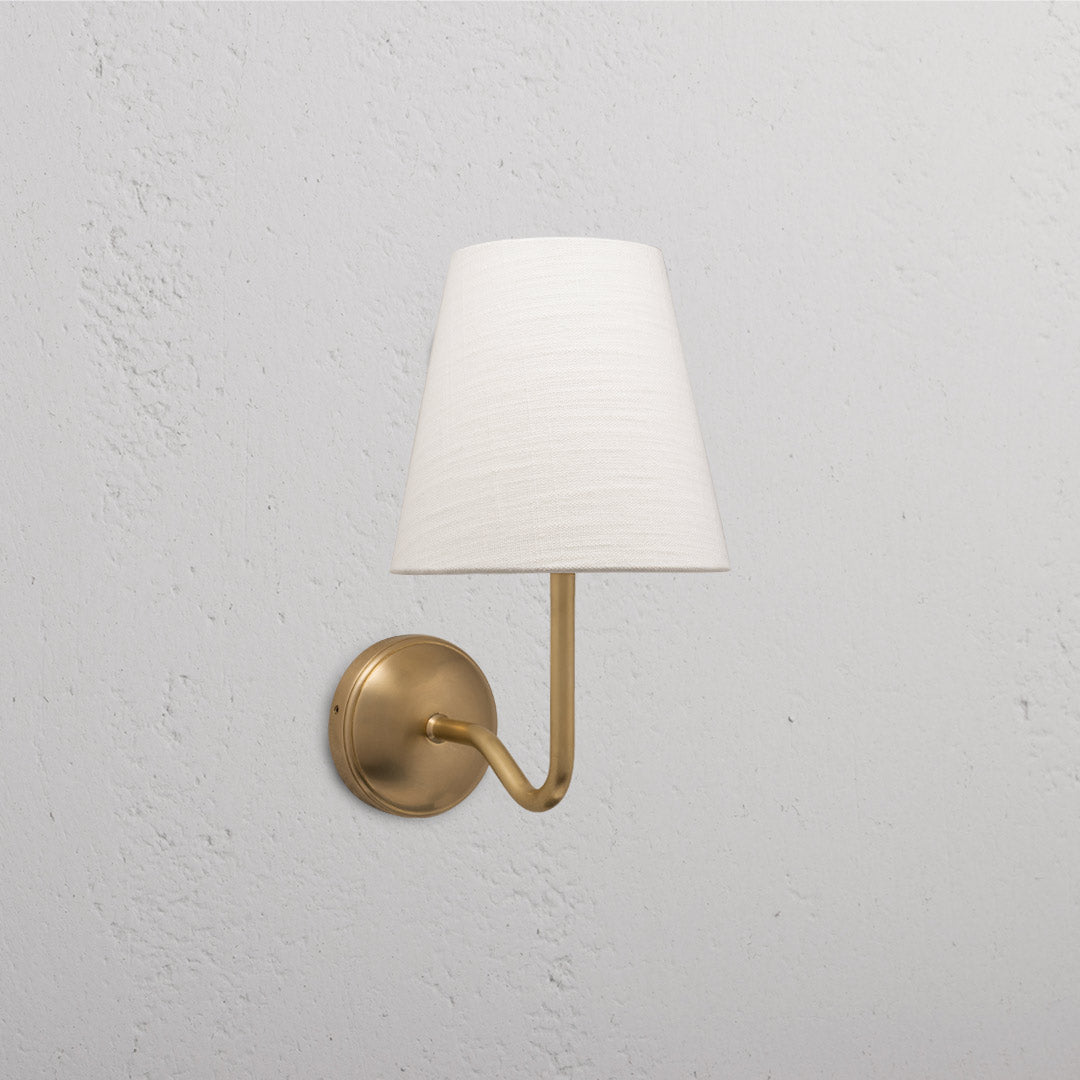 Malvern Medium Wall Light in Alabaster White with Antique Brass finish on a textured white wall.