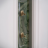 2G Architrave Two Way Toggle Switch in clear antique brass on a decorative green patterned wall.
