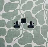 Clear Black Double Socket UK, 2G, mounted on a green and white abstract patterned wall.