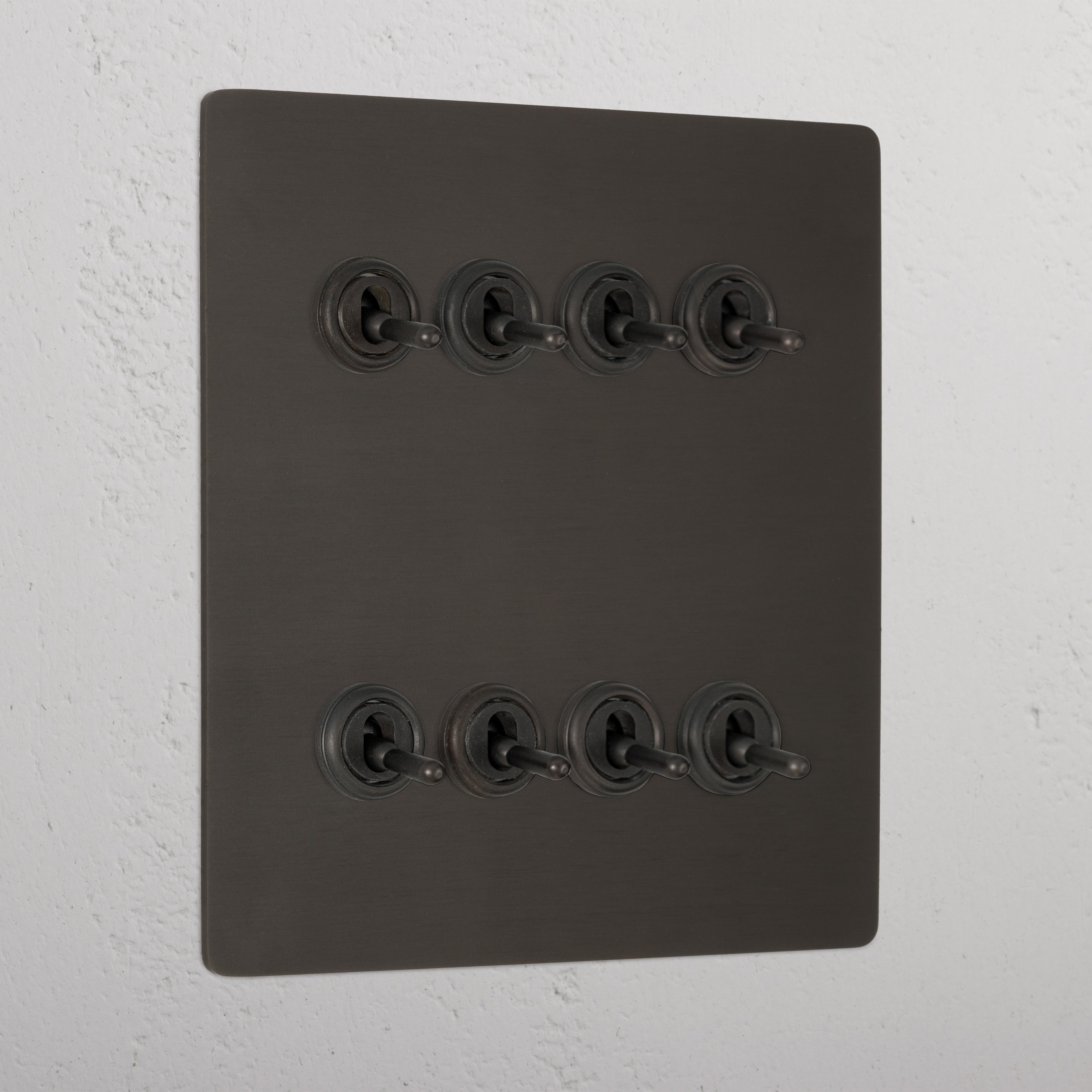 Bronze toggle light switch panel with 8G retractive switches mounted on a textured wall.