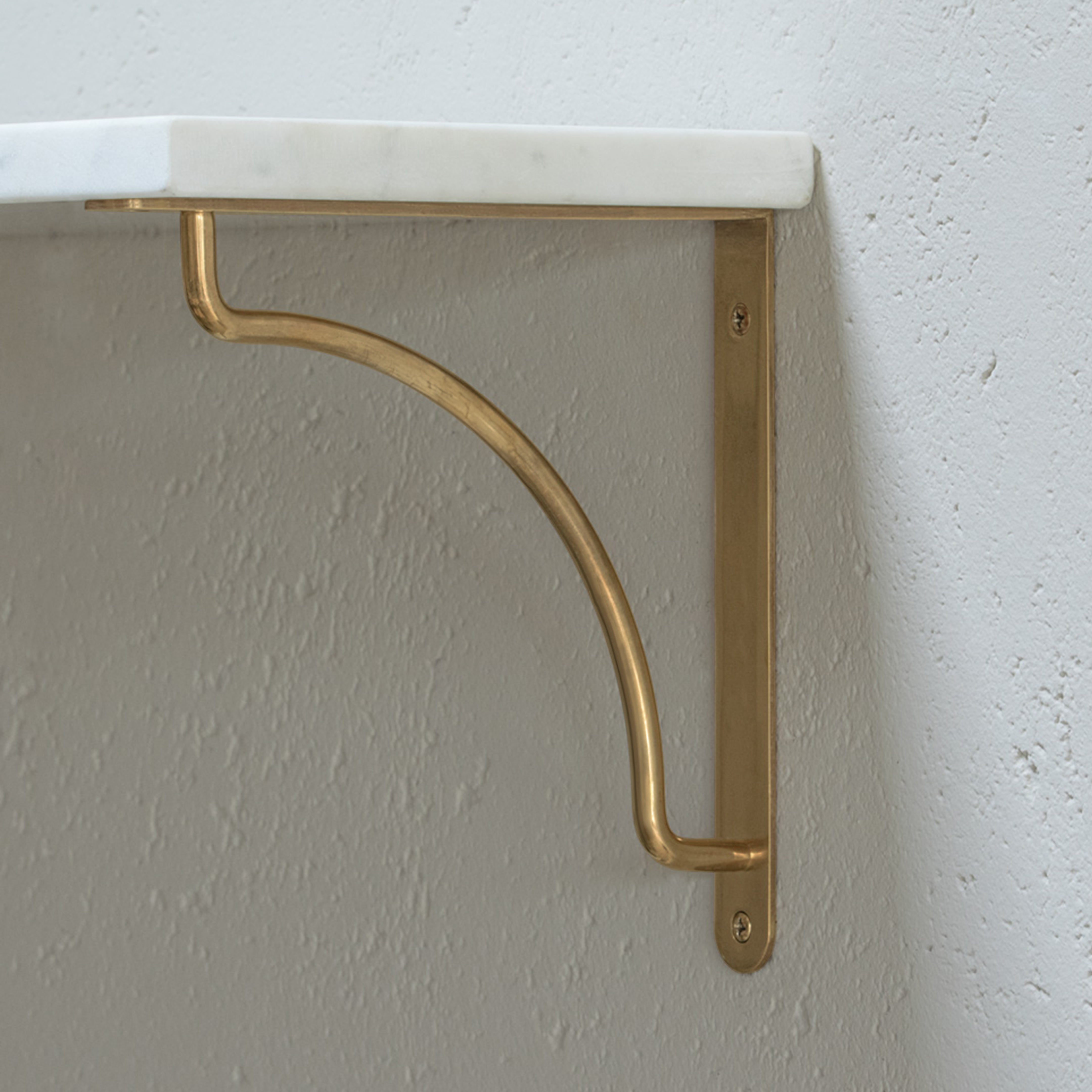 A white marble shelf on Corston Kilburn 200mm antique brass bracket, mounted on a textured white wall.