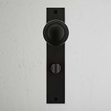 Bronze Poplar Long Plate Sprung Door Knob & Thumbturn on a white wall, featuring a circular design.