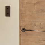 Clayton Flush Rose Sprung Door Handle in bronze on a light wooden door.