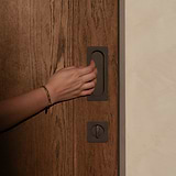 A hand with a bronze bracelet grips a Regent Recessed Medium Pull on a wooden door.