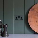 Clear black double socket UK on a dark green wall, with chess-themed decor nearby on a white surface.