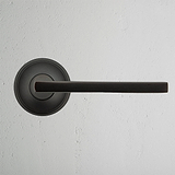 Clayton Sprung Door Handle - Bronze, elegantly designed for easy door operation on a textured white wall.