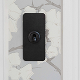Bronze 1G architrave two-way toggle switch on patterned wallpaper, combining classic style with functionality.