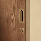 Wooden sliding door with antique brass handle and lock on beige wall.
