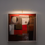 A framed abstract painting in brown, red, and beige tones is lit by a Harrow 580mm antique brass light.
