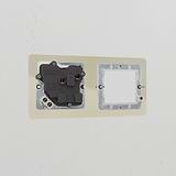 Clear white 1G 50mm module and single socket UK plate, partially installed on a white wall with visible screws.