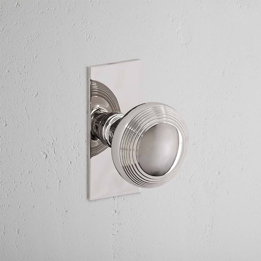 Polished Nickel Poplar Short Plate Fixed Door Knob on white background. Elegant and contemporary design.