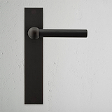 Harper Long Plate Sprung Door Handle - Bronze, shown against a white wall, featuring elegant bronze detailing.