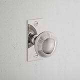 Poplar Short Plate Fixed Door Knob in Polished Nickel on a textured white wall.
