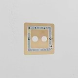 Antique brass 2G switch plate with two circular openings, mounted on a white wall for an elegant look.