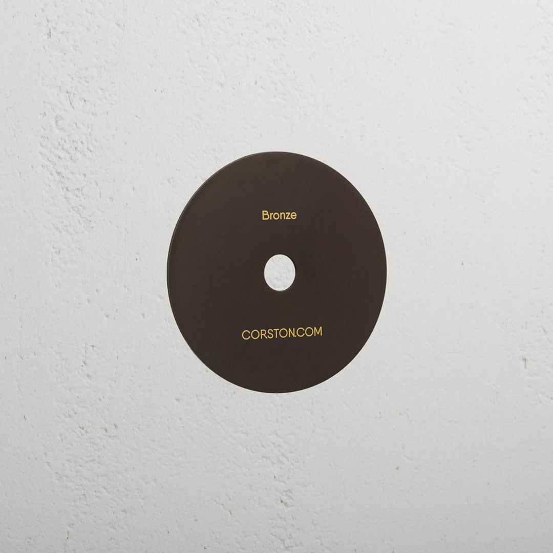 Bronze 'Sample By Finish' disc labeled Bronze' on a textured white surface from the 'Sample Finish - Bronze' collection.