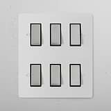 Six 6G Two Way Rocker Switches with paintable polished nickel black finish, arranged in a modern white wall display.
