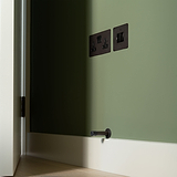 Bronze Black Switched Fused Spur (FCU) on a green wall next to two black electrical outlets and a doorstop.