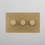 Antique brass 3G two way dimmer switch with three round gold knobs on a white wall.