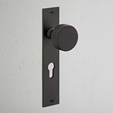 Onslow Long Plate Sprung Door Knob & Euro Lock in bronze, shown against a textured white wall.