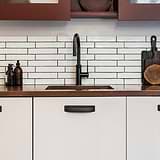 Bronze Elm Cup Handle 164mm on kitchen cabinets with white tile backsplash and wooden countertop accents.