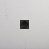 A black square wall socket on a white textured wall with a bronze accent for elegance.