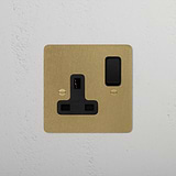 Antique brass black 1G socket with a black switch on a gold-colored plate, mounted on a white wall.