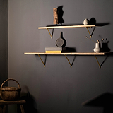Antique brass Brixton shelf bracket 150mm supporting wooden shelves on a dark wall with decor items.