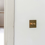 Antique brass 2G two way dimmer switch fixed to off white wall next to off white wooden door panel