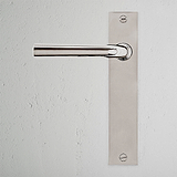 Apsley Long Plate Sprung Door Handle in Polished Nickel on a textured white wall, featuring a sleek rectangular backplate.
