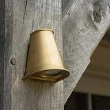 Southwark Mast Light – Antique Brass, a small wall light with conical shape, mounted on weathered wood.