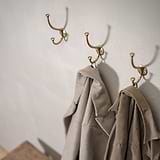 Mews Hook - Antique Brass holding two coats, displayed above a wooden bench. Elegant and functional hooks.