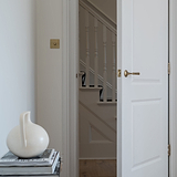 Antique brass Digby Sprung Door Handle on an open white door, with a glimpse of a staircase in the background.