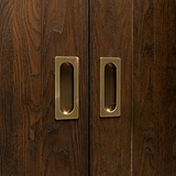 Close-up of two Regent Recessed Medium Pull handles in antique brass on dark wooden sliding doors.