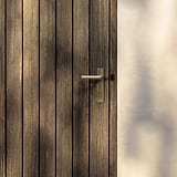 Apsley Long Plate Sprung Door Handle in antique brass on a wooden door with vertical planks.