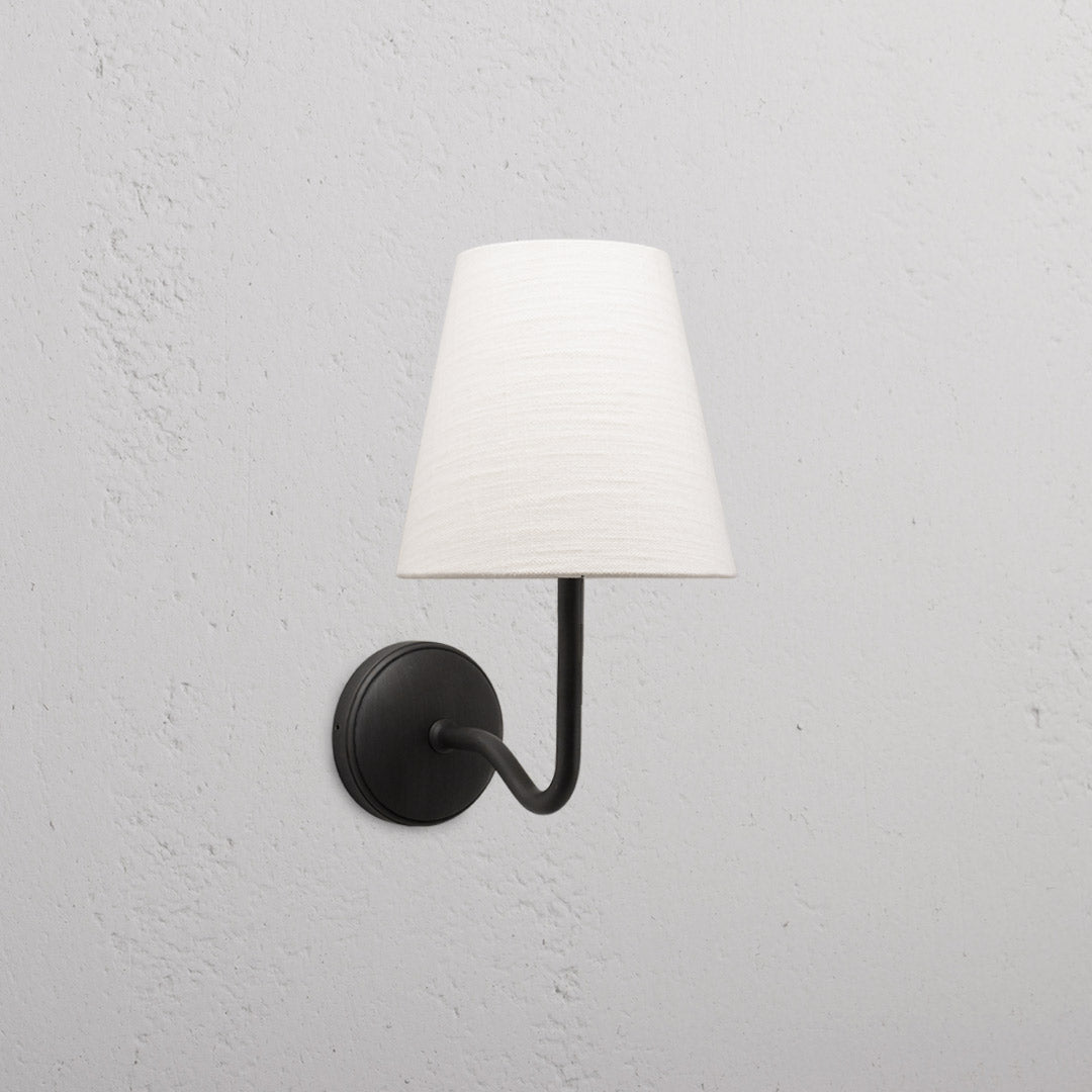 Malvern Medium Wall Light Alabaster White with bronze finish, featuring a conical shade mounted on a textured wall.