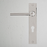 Harper Long Plate Sprung Door Handle & Euro Lock in polished nickel on a textured white wall.