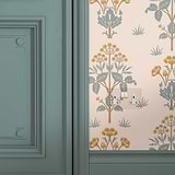 Clear white double socket painted pastel green fixed to wall with pastel green and orange floral wallpaper next to pastel green wooden door