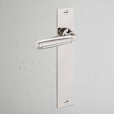 Polished nickel Digby Long Plate Sprung Door Handle on a rectangular backplate against a light grey wall.