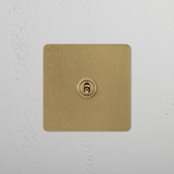Antique Brass 1G Retractive Toggle Switch for 1G Switches & Dimmers on a textured white wall.