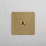 Antique brass 1G centre retractive toggle switch on a white textured wall.