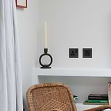 Bronze Black Single Socket UK, 1G, on a white wall in a modern interior with rattan chair and decor.