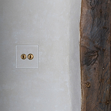 2G Two Way Toggle Switch in clear antique brass on a white wall near a wooden beam, part of 2G Switches & Dimmers.