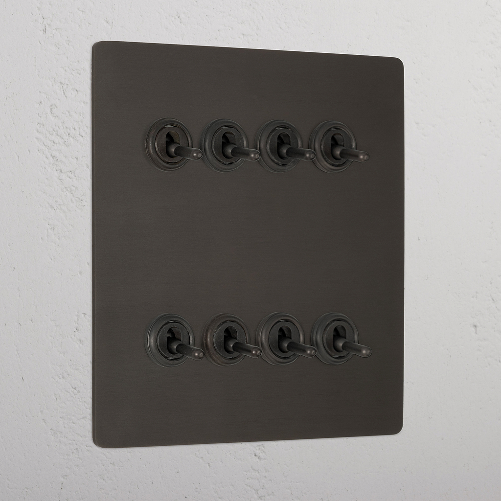 Bronze toggle light switch panel with 8G retractive switches mounted on a textured wall.