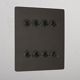 Bronze toggle light switch panel with 8G retractive switches mounted on a textured wall.